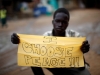 A young South Sudanese boy who works cleaning shoes in the streets holds a sign stating 